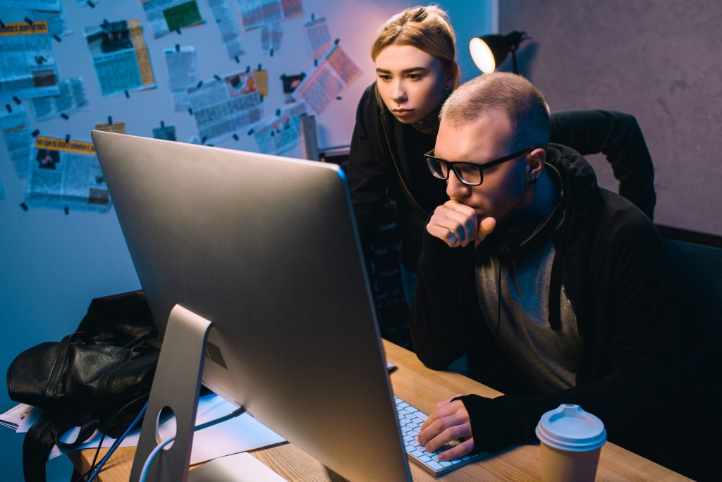 serious couple of hackers working with computer together in dark room